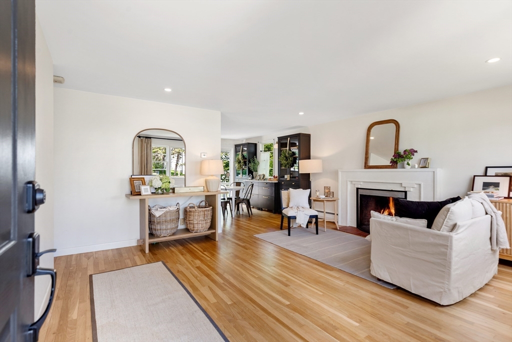 Living room with hardwood floors, a white sofa, and a lit fireplace opening to the dining area.