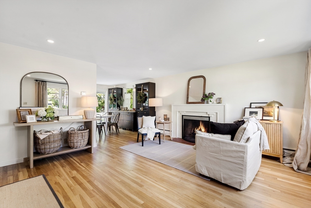Living room with a lit fireplace, white seating, and hardwood floors.