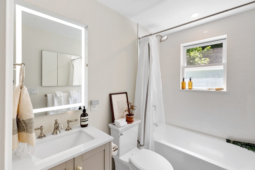 Bright bathroom with a white vanity, large mirror, and bathtub beneath a window.