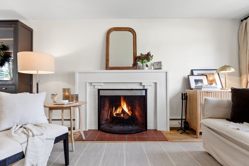 Living room with a lit brick fireplace, white mantel, light sofas, and a pale rug.