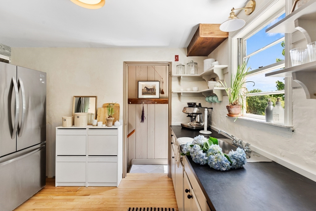 Bright kitchen with black countertops, white open shelving, and hydrangeas beside the sink.