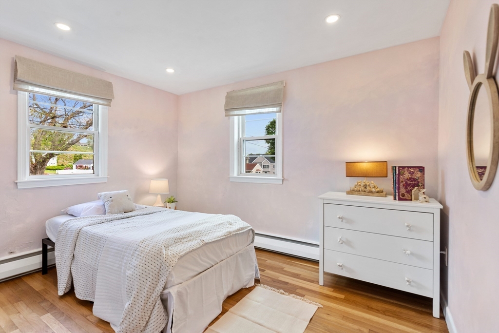 Bedroom with a white bed, pale pink walls, two windows, and hardwood floors.