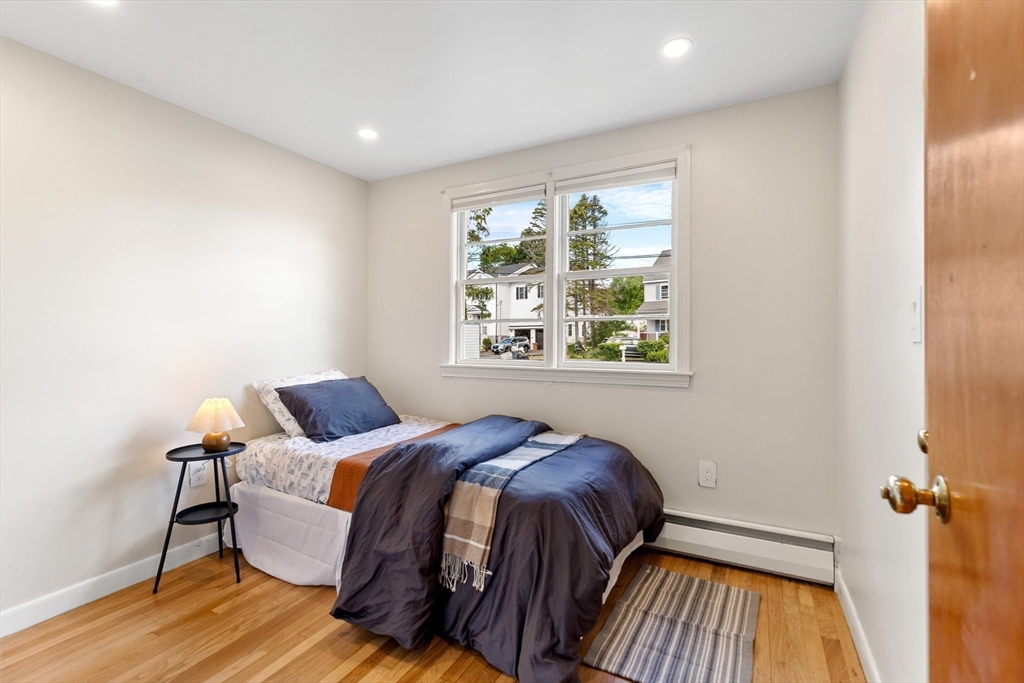Staged bedroom with navy bedding, hardwood floors, and a double window overlooking neighboring homes.