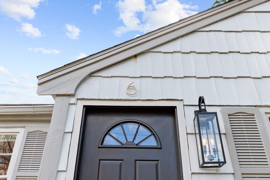 Front entrance with a dark fanlight door, white shingle siding, and house number 6.