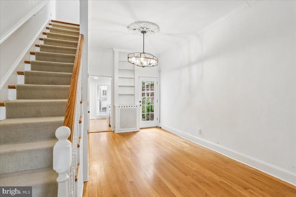 Empty entry hall with hardwood floors, built-in shelves, and a carpeted staircase.