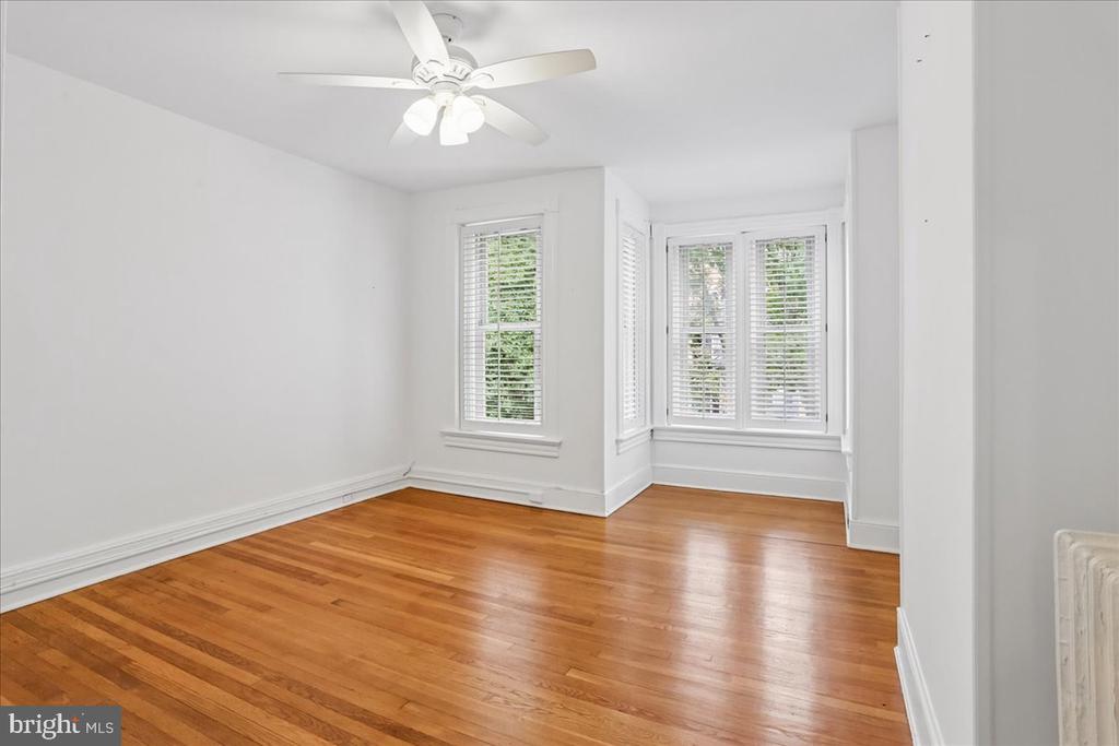 Bright empty room with hardwood floors, a ceiling fan, and windows with blinds.