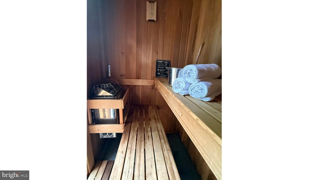 Wood-paneled sauna with tiered benches, a heater, and rolled towels.