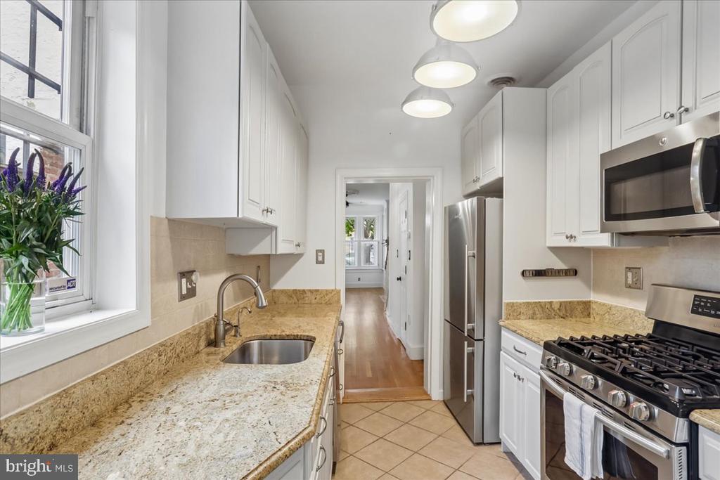 Kitchen with white cabinets, tan stone counters, stainless-steel appliances, and a window above the sink.
