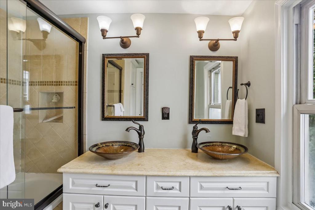 Bathroom with a double vanity, decorative vessel sinks, and a glass-enclosed tiled shower.