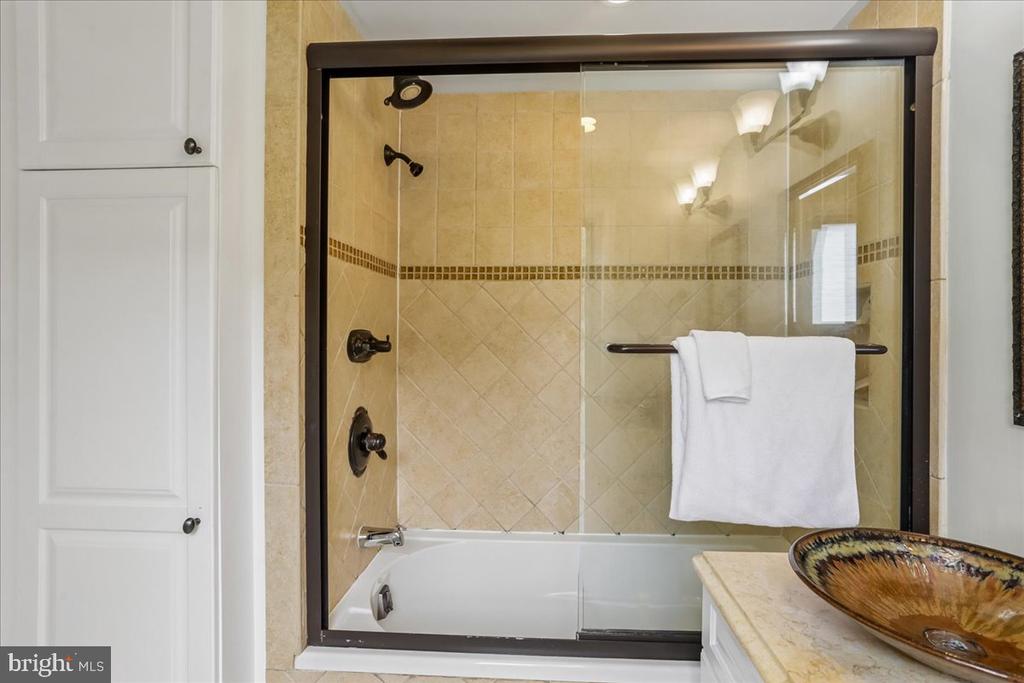 Bathroom with a glass-enclosed tub, beige tile, dark fixtures, and a vessel sink.