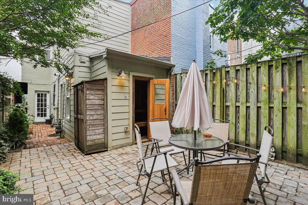 Rear courtyard patio with brick paving, outdoor dining set, and wooden privacy fence.