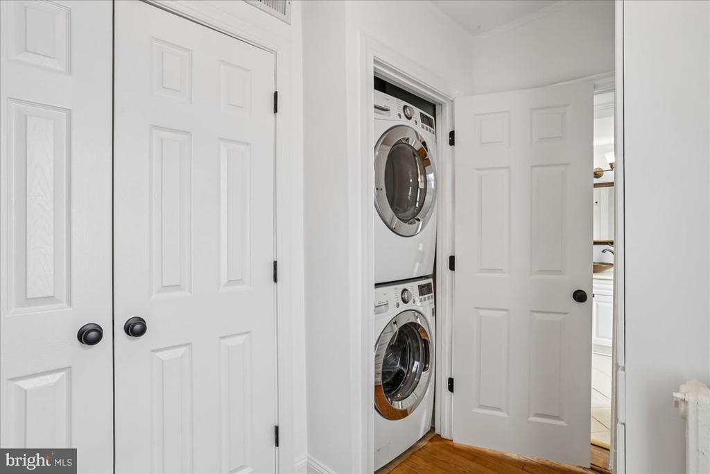 Laundry closet with stacked front-loading washer and dryer behind an open white door.