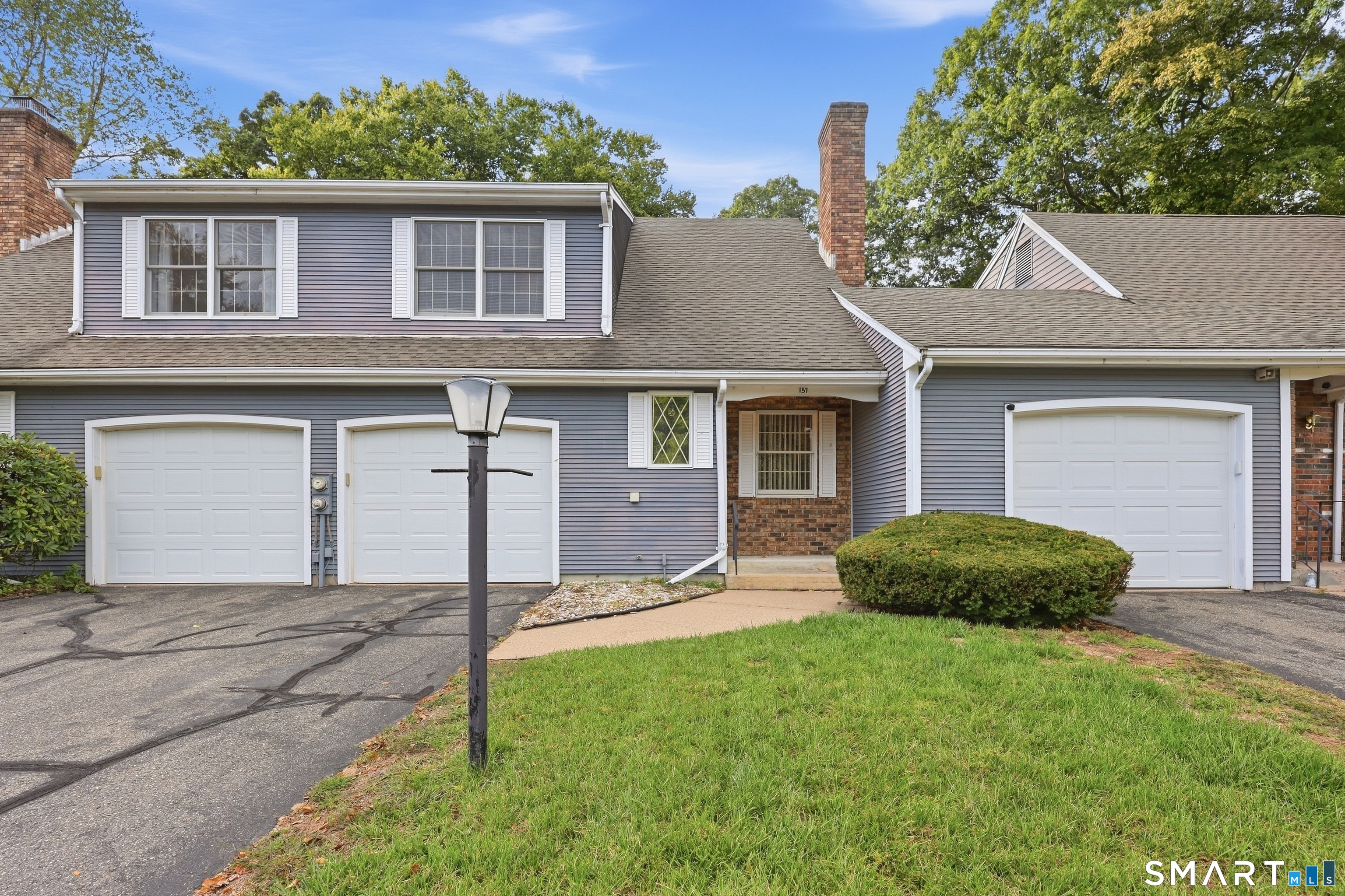 Gray-sided house with a brick entry, multiple garage doors, and a front lawn.