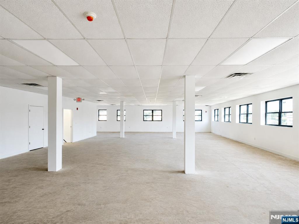 Vacant open office with beige carpet, white columns, and rows of windows.