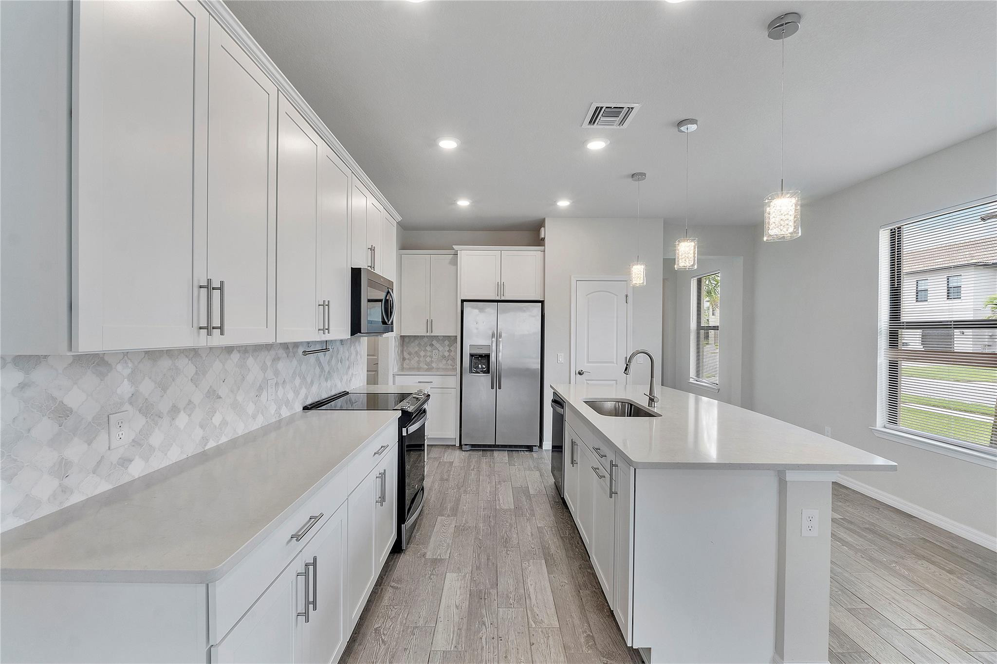 Modern white kitchen with stainless steel appliances, patterned backsplash, and a large island with sink.
