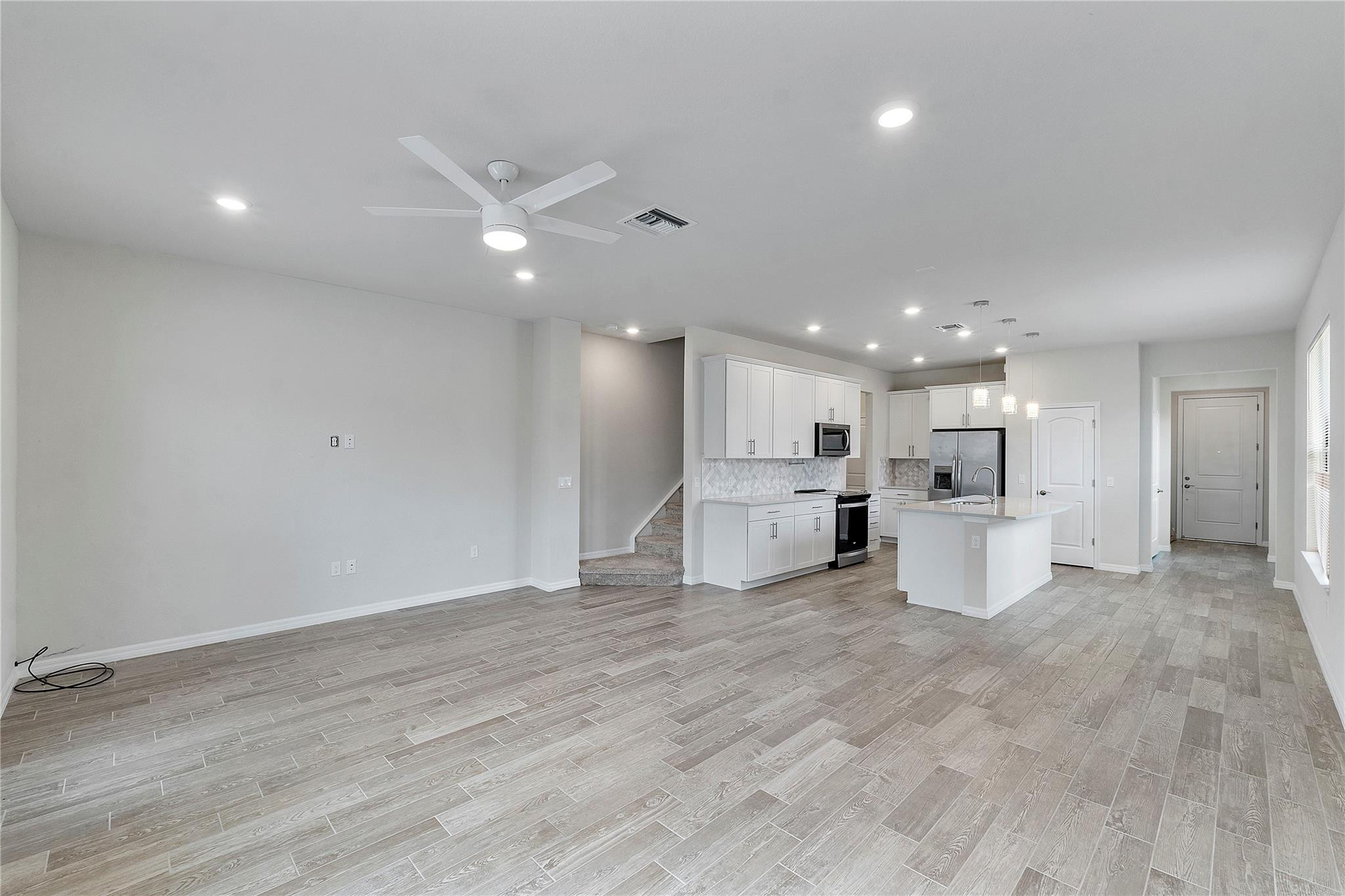 Open-plan kitchen and living area with a white island and gray wood-look tile flooring.