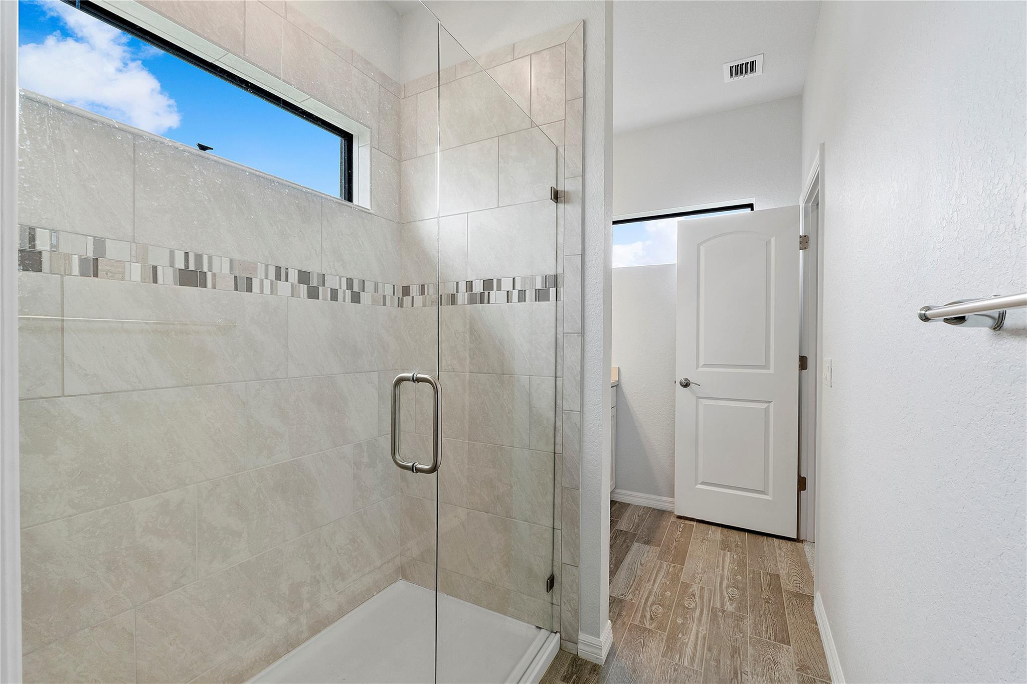 Walk-in shower with glass enclosure, tiled walls, mosaic accent band, and a high window.