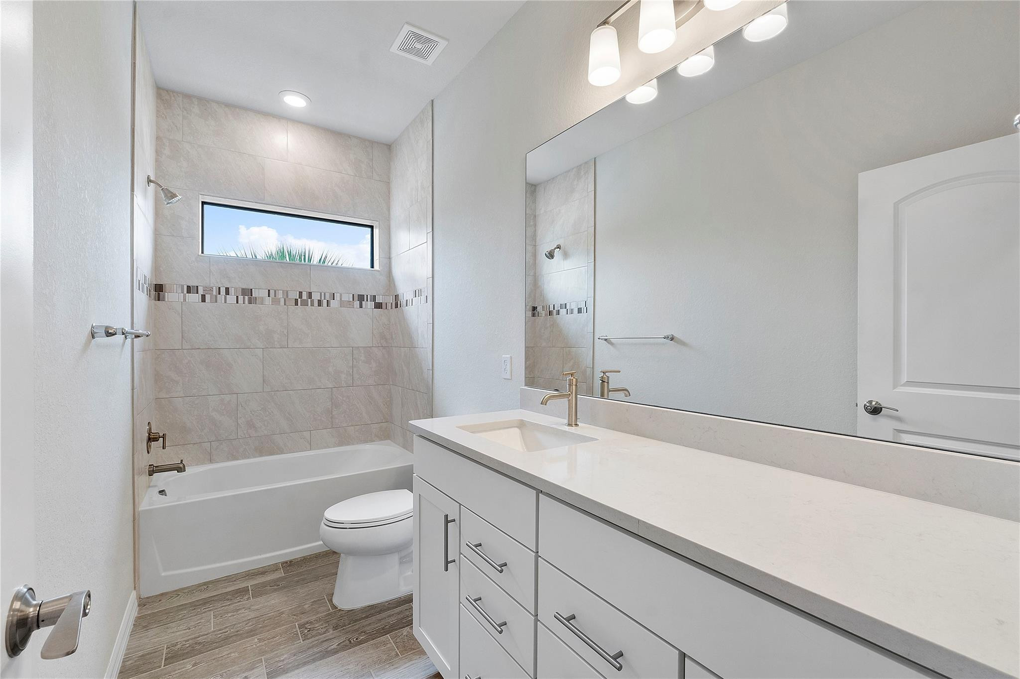 Modern bathroom with a white vanity, tiled bathtub surround, and narrow horizontal window.
