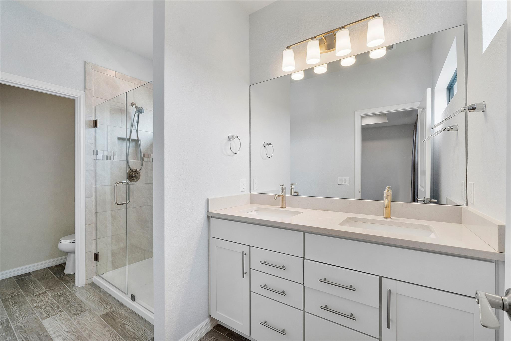 Bathroom with a double-sink vanity, large mirror, and glass-enclosed tiled shower.