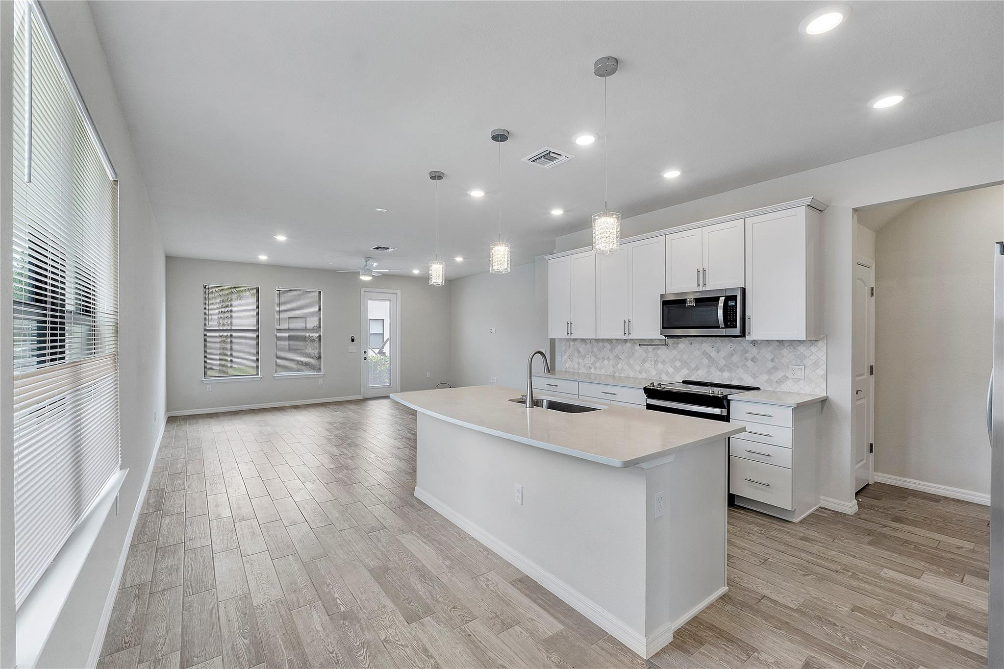 Unfurnished kitchen with a large white island, white cabinets, and wood-look tile flooring.