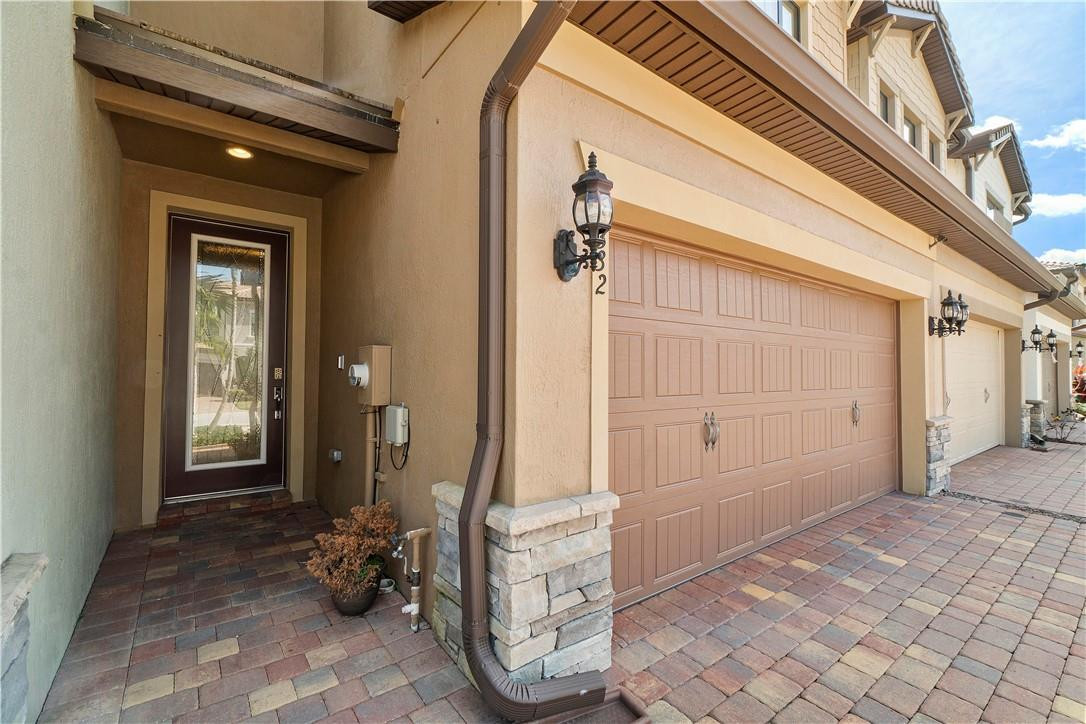 Home exterior with a recessed entry, tan garage door, stone-trimmed columns, and paver driveway.