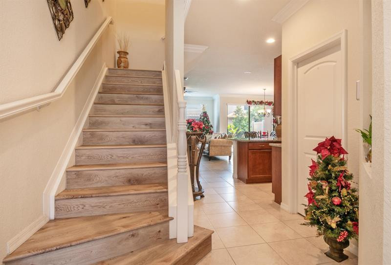 Home entryway with a wood-look staircase opening onto a tiled kitchen and living area decorated for Christmas.