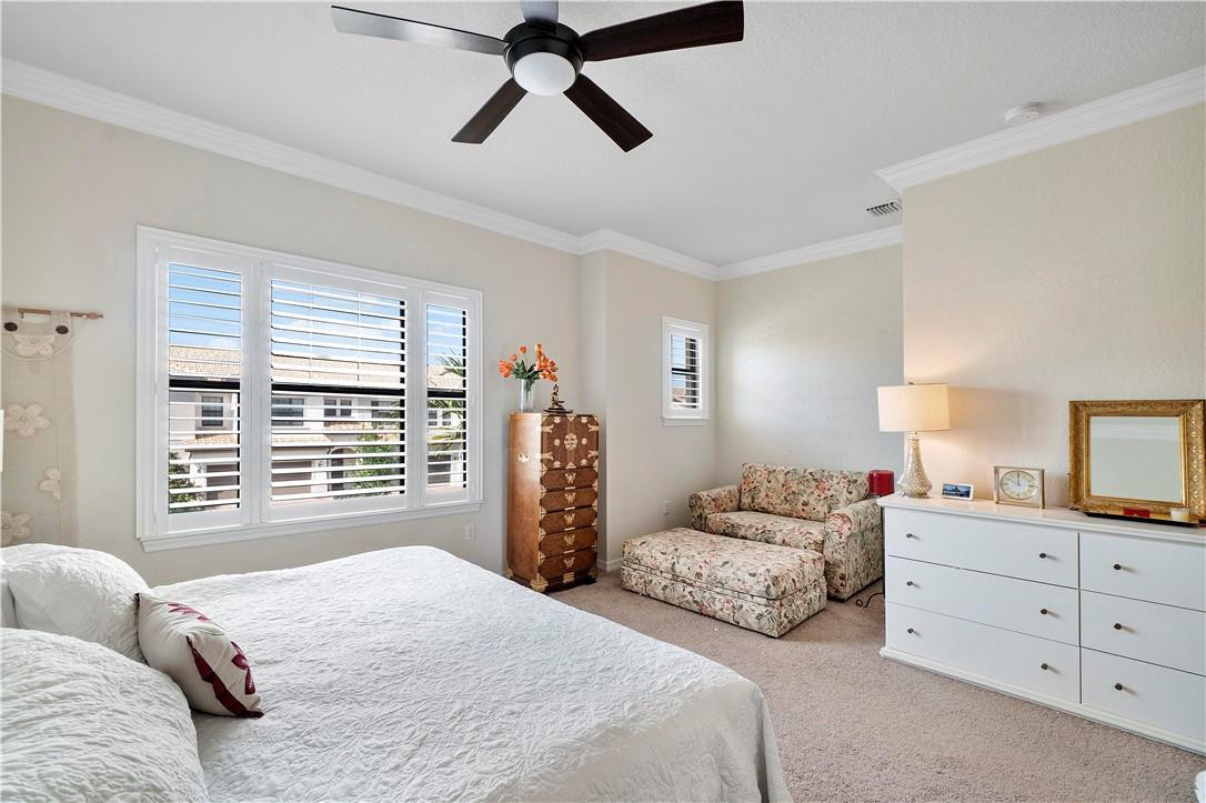 Furnished bedroom with a large bed, plantation shutters, floral loveseat, and ceiling fan.