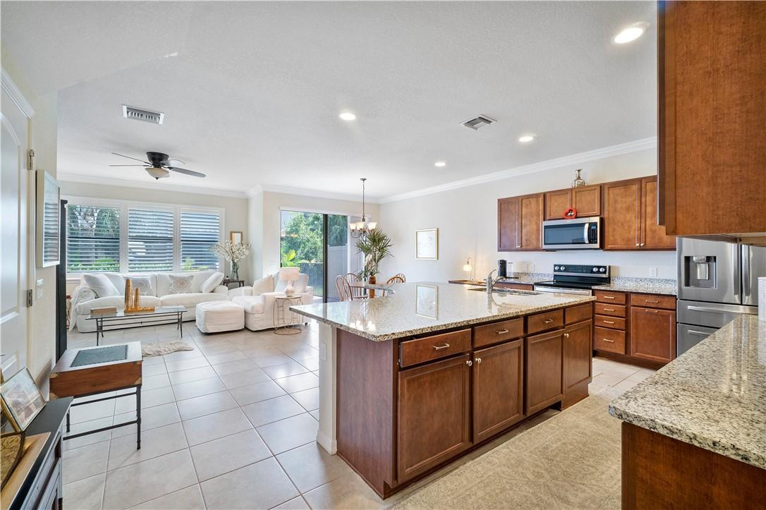 Open-plan kitchen with a granite island, wood cabinets, stainless steel appliances, and an adjoining bright living area.