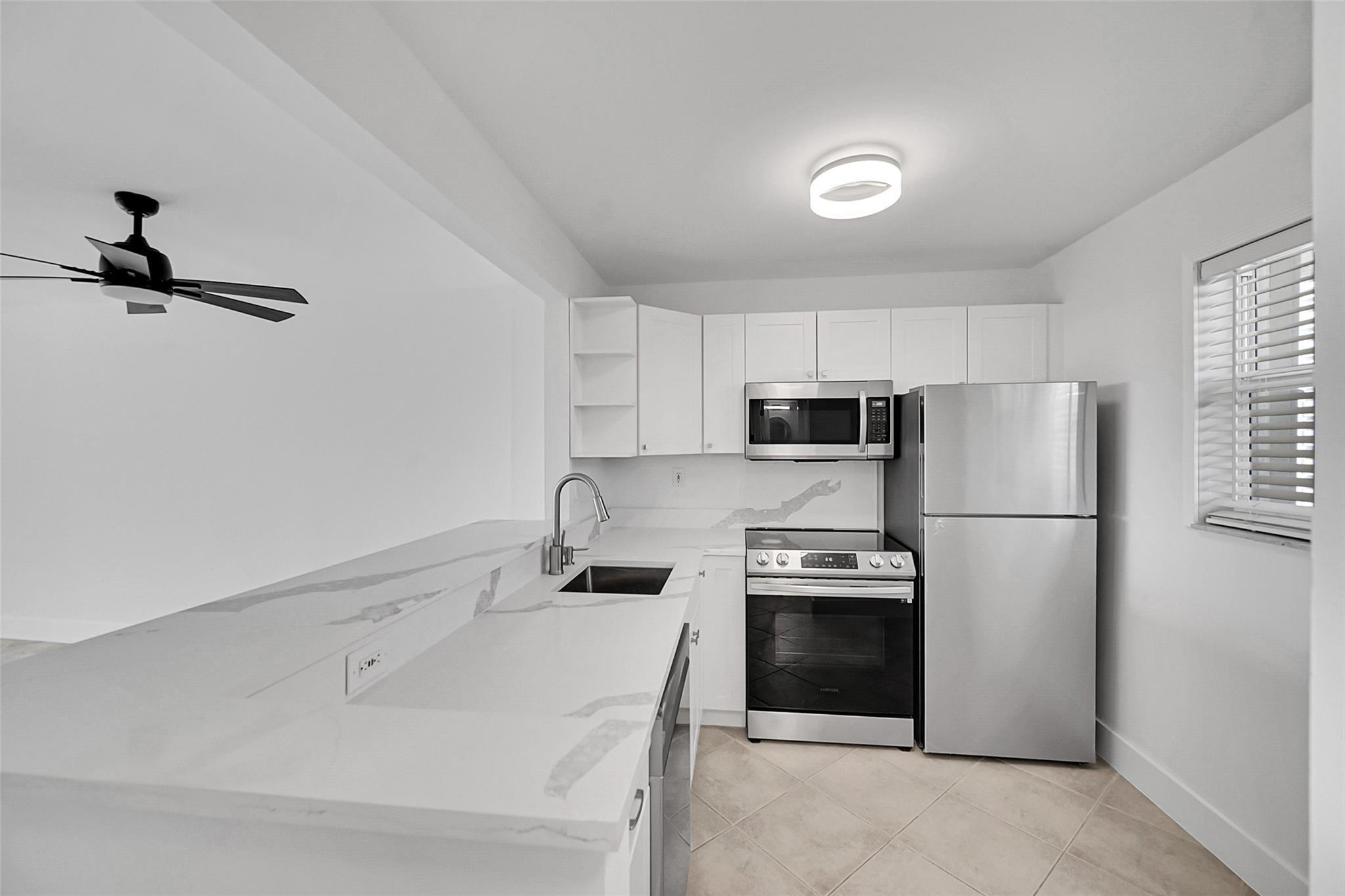 White kitchen with marble-look counters, stainless steel appliances, and plantation shutters.