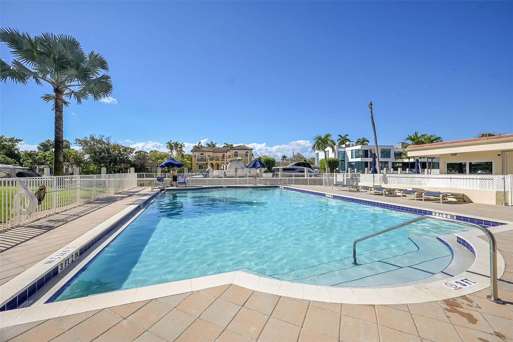 Outdoor pool with a shallow entry shelf, metal handrails, and lounge chairs along the deck.