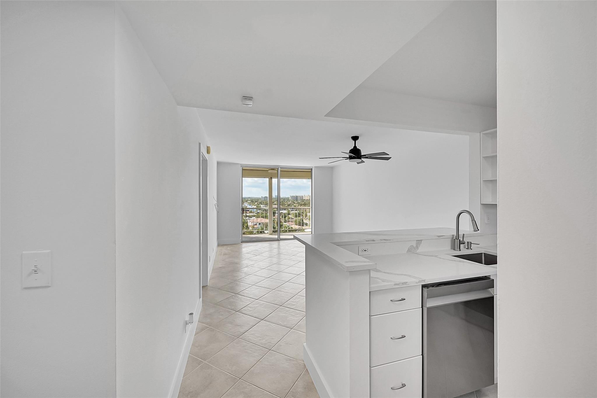 Open kitchen with white peninsula and stainless-steel dishwasher, facing sliding doors to a balcony.