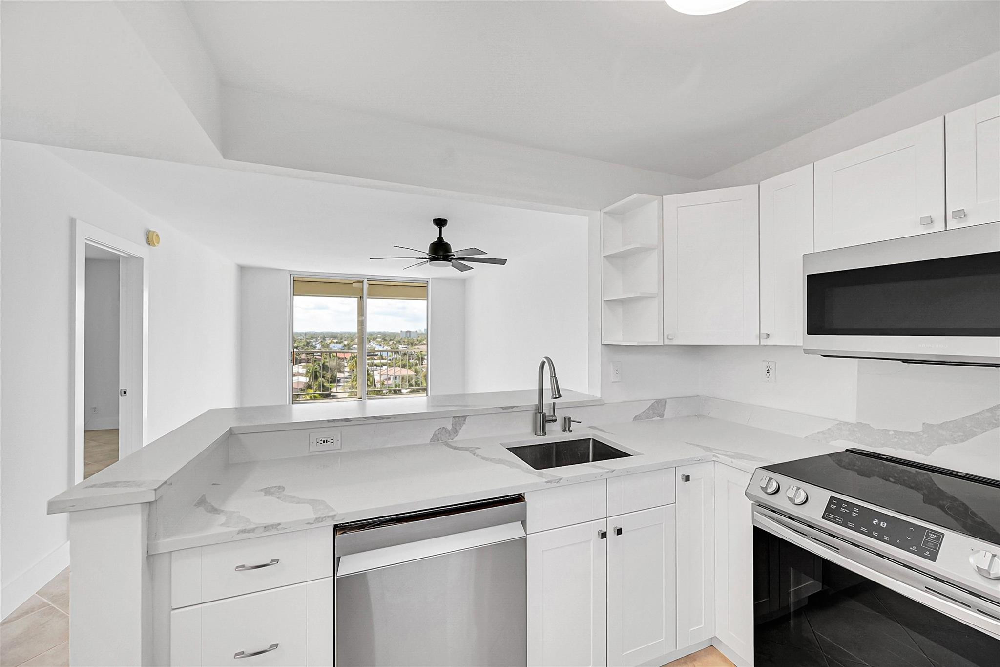 Bright white kitchen with veined stone counters, stainless steel appliances, and a balcony view.