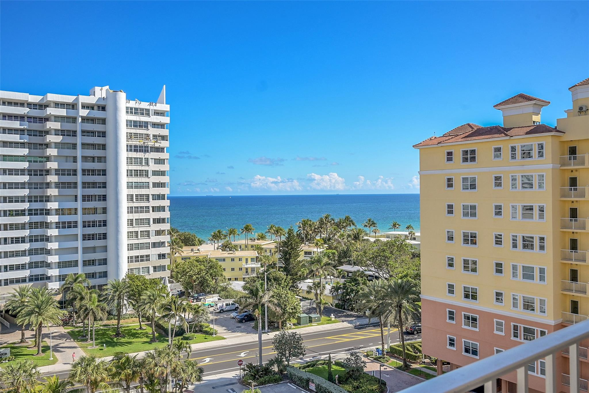 Ocean view between coastal condominium towers, with palm-lined beachfront and a balcony railing.