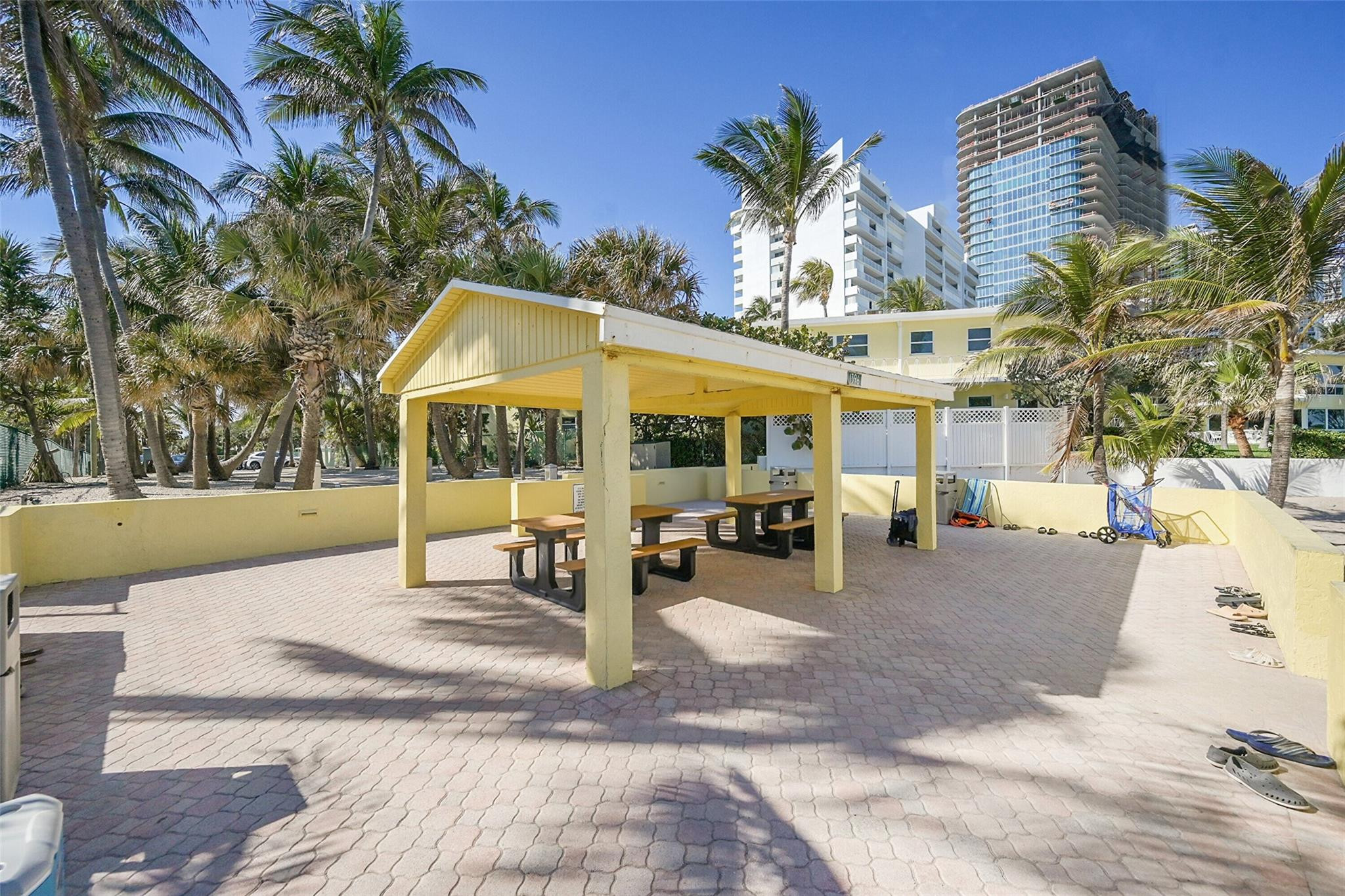 Outdoor patio with a yellow picnic pavilion, tables, palm trees, and condominium towers.