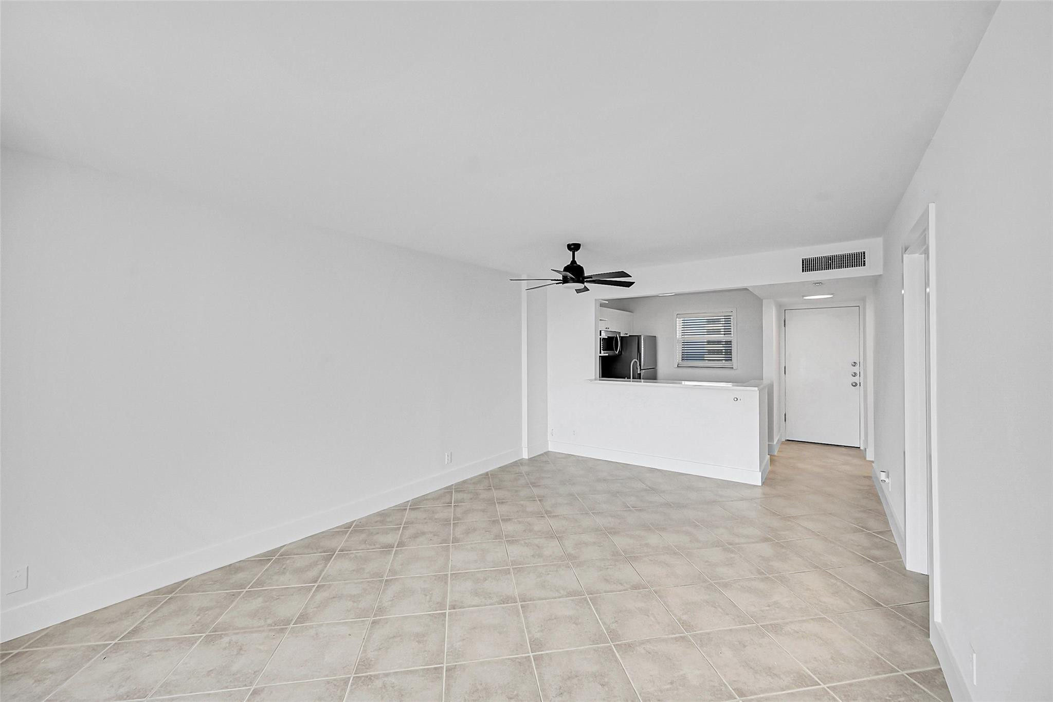 Vacant tiled living area with a ceiling fan and pass-through to the kitchen.