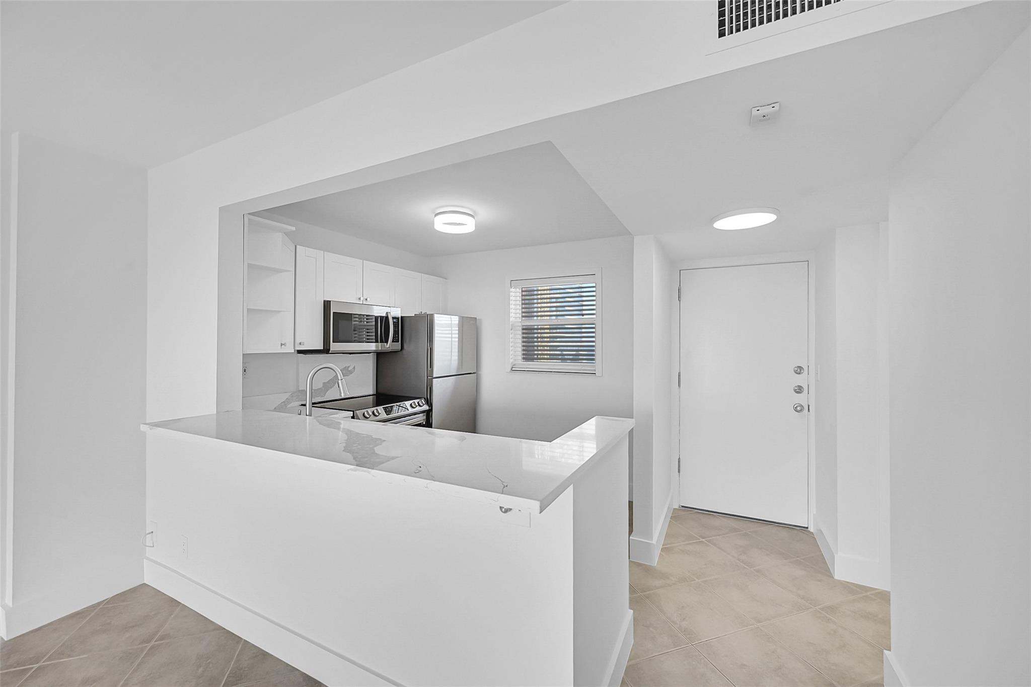Unfurnished white kitchen with a stone peninsula, stainless appliances, and beige tile floor.