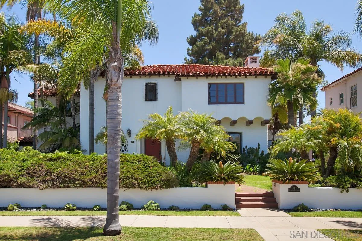 White Spanish-style home with a red tile roof, palm trees, and landscaped front entry.
