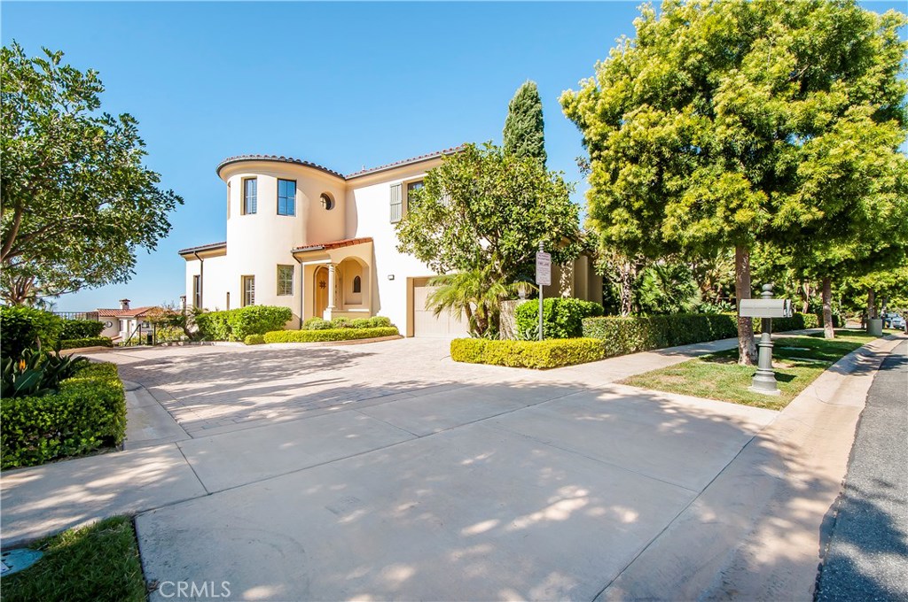 Two-story home with a rounded tower, arched entry, broad driveway, and mature landscaping.