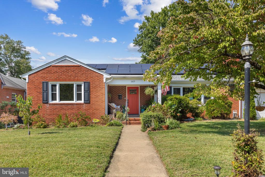 Red brick single-story home with solar panels, black shutters, and a red front door.