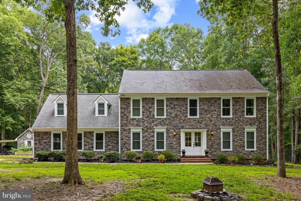 Two-story stone house with white trim and a wooded, tree-shaded front yard.