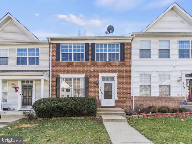 Brick townhouse with a front lawn, shrubs, and a concrete walkway between white-sided homes.