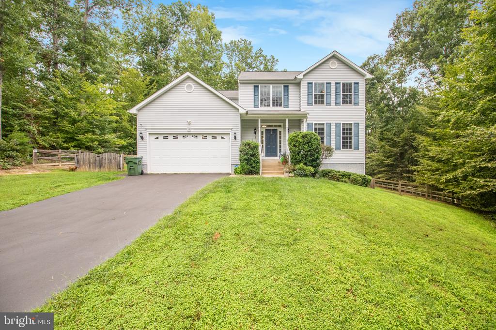 Two-story white home with blue shutters, attached garage, and a broad lawn bordered by trees.