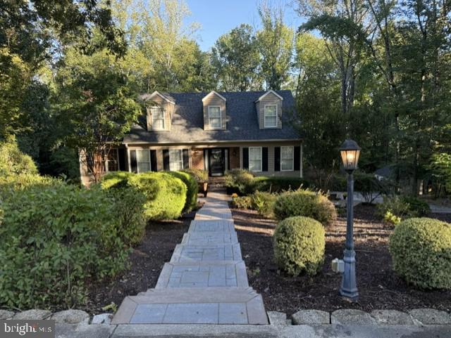 Two-story house with dormer windows, a covered porch, and a stone walkway through landscaped gardens.