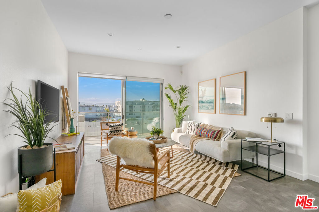 Bright living room with a white sofa, layered patterned rugs, and sliding glass doors to a balcony.