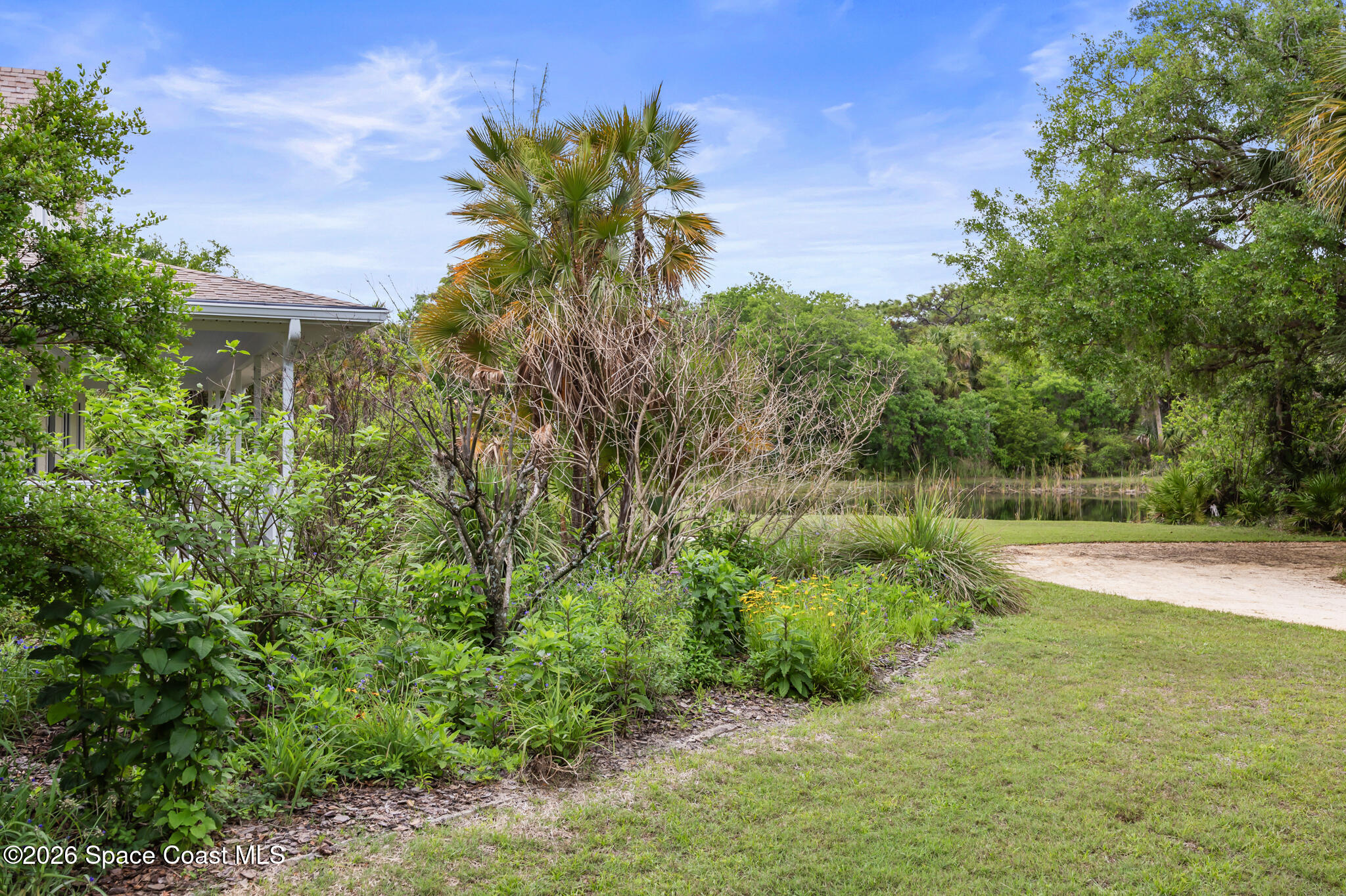 Landscaped yard with a pond, palms, flowering plants, and part of the house.