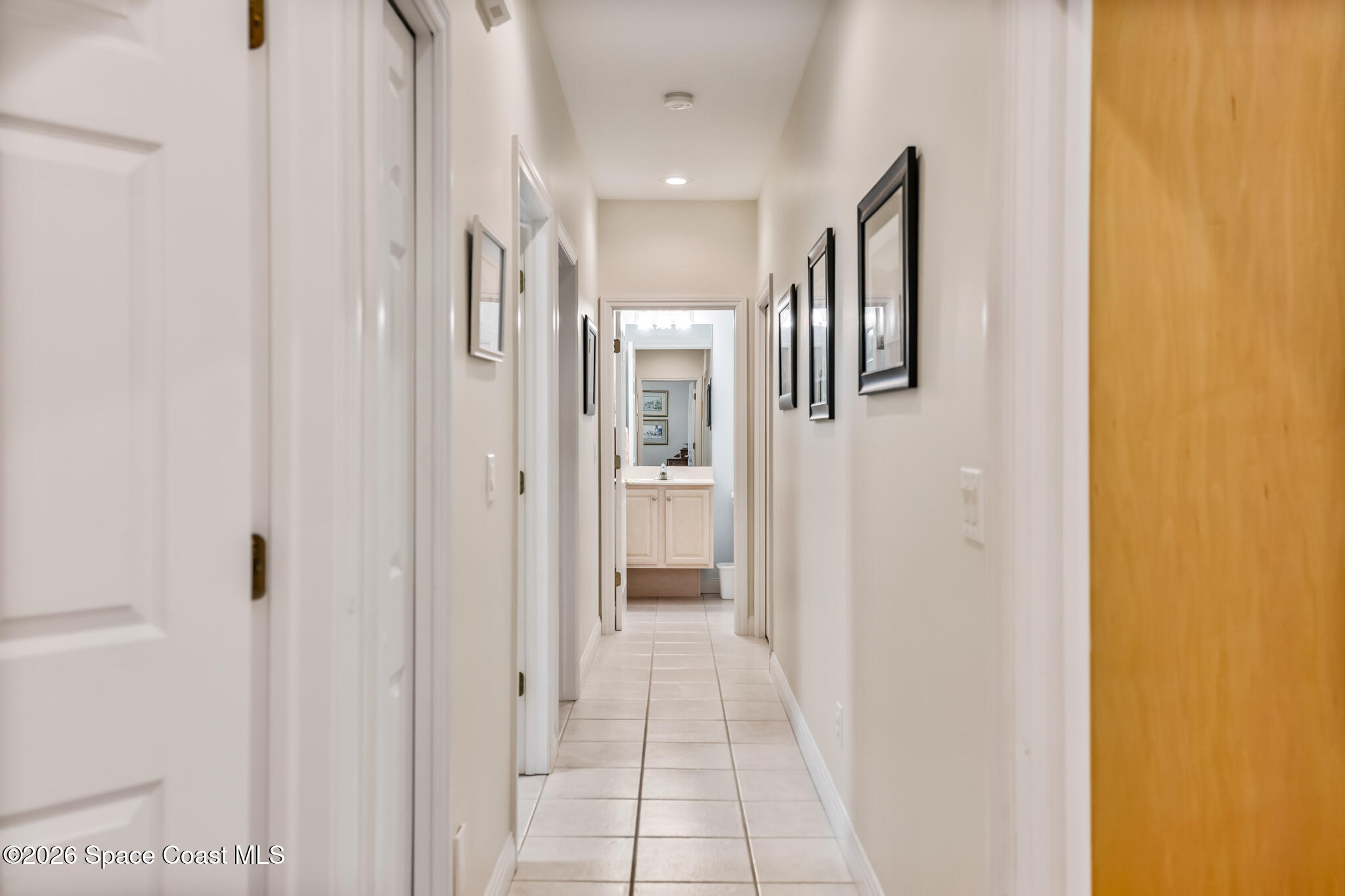Long tiled hallway with framed pictures and a bathroom vanity at the far end.