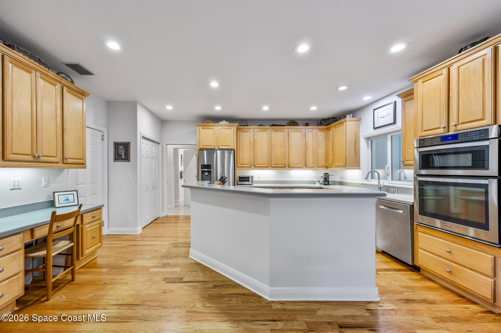 Kitchen with honey-colored cabinets, a large island, stainless-steel appliances, and hardwood floors.