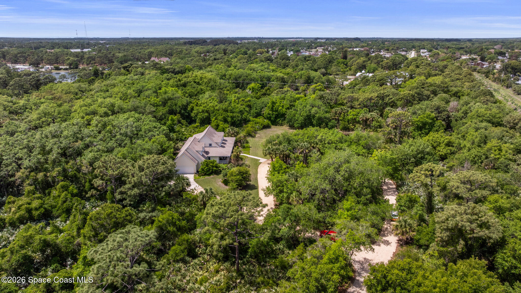 Aerial view of a house amid dense trees, with a long curved driveway.