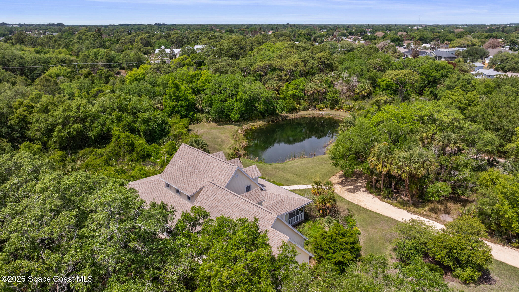 Aerial view of a home beside a pond, surrounded by trees and lawn.