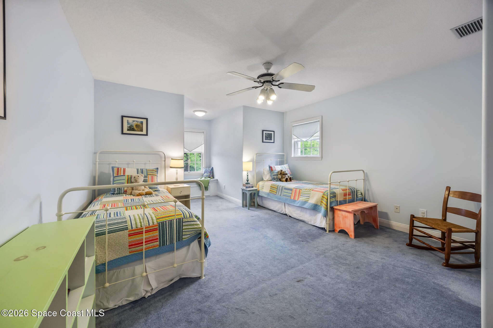 Furnished bedroom with two twin beds, colorful striped quilts, and a ceiling fan.